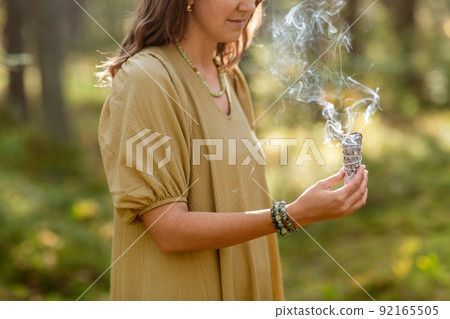 woman with sage performing magic ritual in forest 92165505