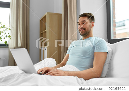 man with laptop in bed at home bedroom 92165621