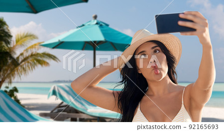 smiling woman in bikini taking selfie on beach 92165693