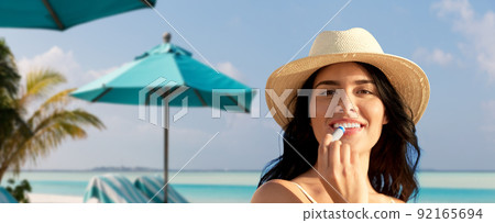 smiling woman in bikini with lip balm on beach 92165694