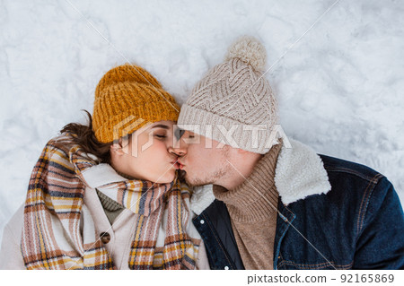 happy couple kissing lying on snow in winter happy couple kissing lying on snow in winter 92165869