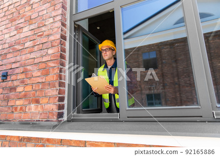 male builder with clipboard looking out window male builder with clipboard looking out window 92165886