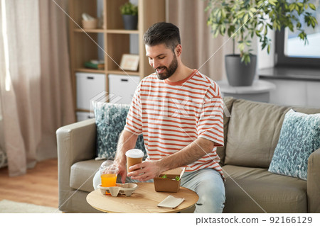 smiling man with takeaway food and drinks at home 92166129