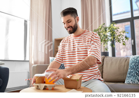 smiling man with takeaway food and drinks at home smiling man with takeaway food and drinks at home 92166135