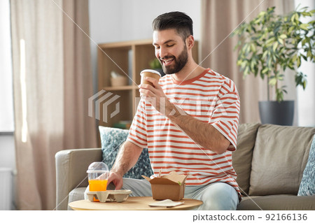 smiling man with takeaway food and drinks at home smiling man with takeaway food and drinks at home 92166136
