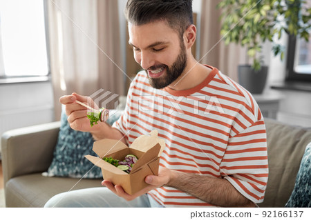 smiling man eating takeaway food at home 92166137