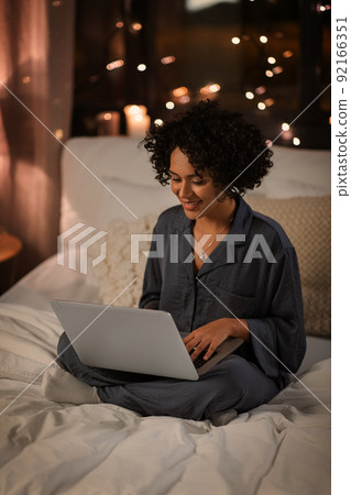 happy woman with laptop sitting in bed at night 92166351