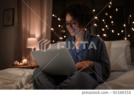 happy woman with laptop working in bed at night 92166358