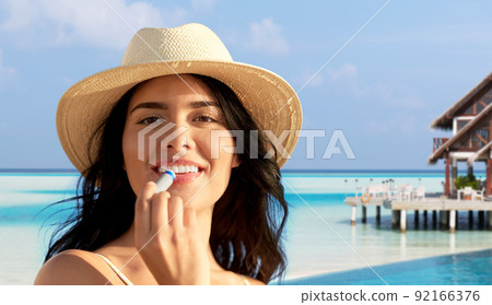 smiling woman in bikini with lip balm on beach 92166376