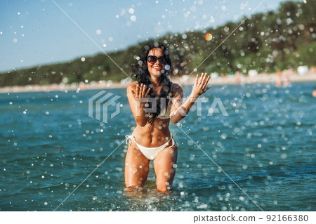 woman in bikini splashing sea water on beach woman in bikini splashing sea water on beach 92166380
