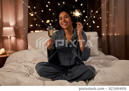 happy woman drinking champagne in bed at night 92166409