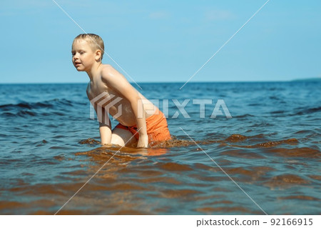 7-8 years old cute caucasian boy going out from the sea to the shore tired. 92166915