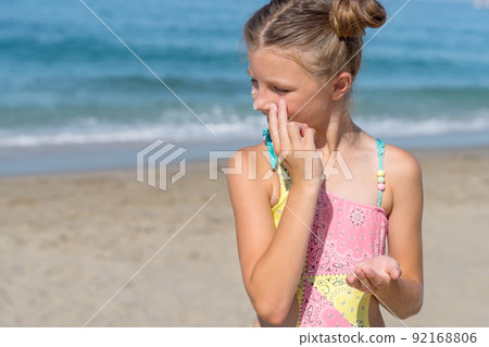 A young girl applies sunscreen to her body on the beach. A young girl applies sunscreen to her body on the beach. 92168806