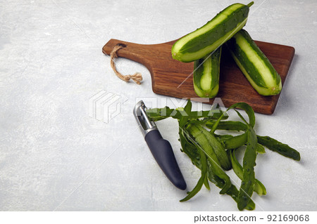 Fresh cucumbers with skin and knife on a brown wooden cutting board on a light gray concrete table 92169068