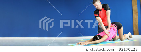 Man helping woman stretching back on mat, shared yoga class in morning Man helping woman stretching back on mat, shared yoga class in morning 92170125