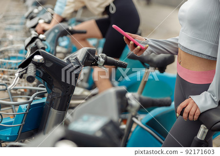 Close up of sportive woman renting bicycle in bike sharing city service using mobile phone 92171603