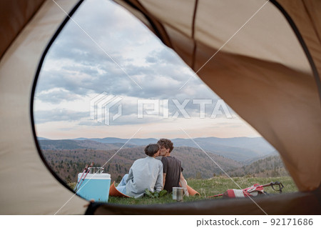 View from inside tent on beautiful landscape of mountains and couple kissing. Love and travel. View from inside tent on beautiful landscape of mountains and couple kissing. Love and travel. 92171686