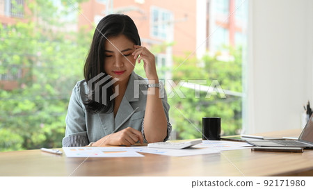 Serious businesswoman analyzing marketing research reports at her office desk 92171980