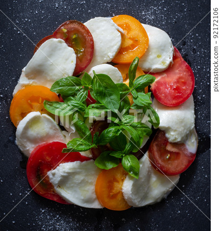 Homemade caprese salad with mozzarella, tomatoes and basil on slate. Top view. 92172106