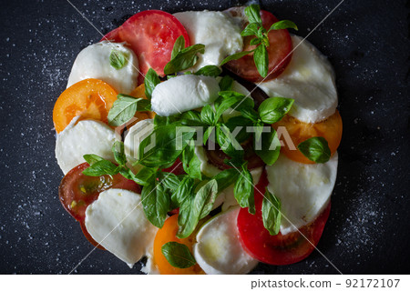 Homemade caprese salad with mozzarella, tomatoes and basil on slate. Top view. 92172107