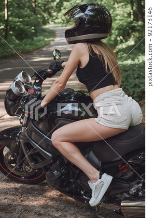 Young woman biker in a helmet sitting on a motorcycle in the underground parking garage Young woman biker in a helmet sitting on a motorcycle in the underground parking garage 92173146