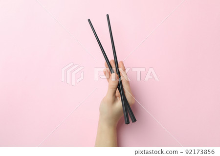 Female hand holding chopsticks on pink background Female hand holding chopsticks on pink background 92173856