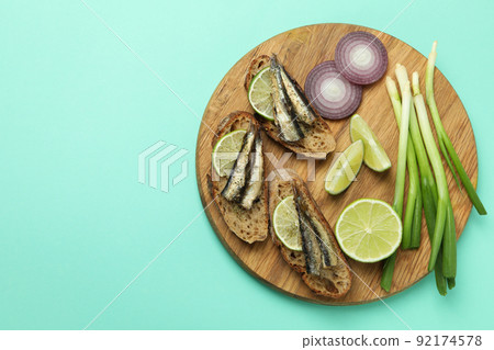Board with sandwiches with sprats on mint background 92174578