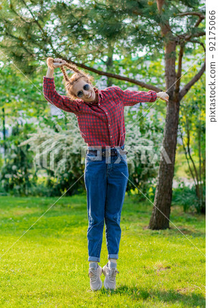Cheerful woman lifts herself into the air by pigtails in a green park Cheerful woman lifts herself into the air by pigtails in a green park 92175066