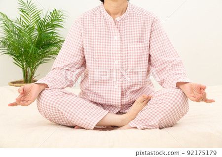 Middle-aged woman wearing pajamas and meditating in the bedroom 92175179