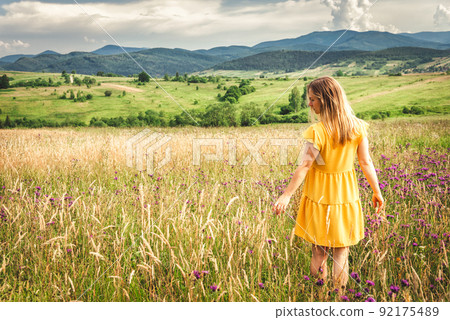 Woman in yellow dress staying at the green meadow in the mountain 92175489