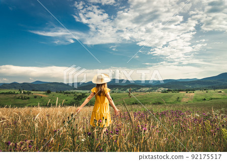 Woman in yellow dress and hat staying at the green meadow in the mountain 92175517
