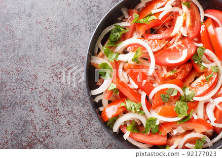 Delicious homemade tomato salad with onion and cilantro seasoned with olive oil close-up in a plate. Horizontal top view 92177023