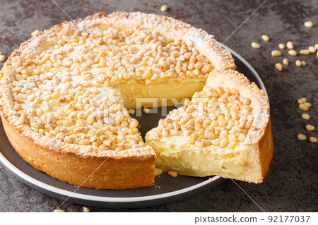 Torta della Nonna is the most delicious Italian custard tart made with sweet shortcrust pastry, custard cream and topped with pine nuts closeup in the plate. Horizontal 92177037