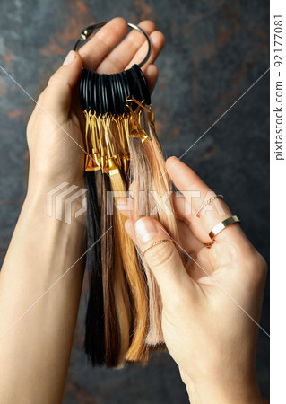 Female hand holds hair samples on dark background 92177081