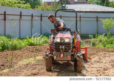A man on a mini-excavator levels a piece of land, loosens the soil. A man on a mini-excavator levels a piece of land, loosens the soil. 92177982