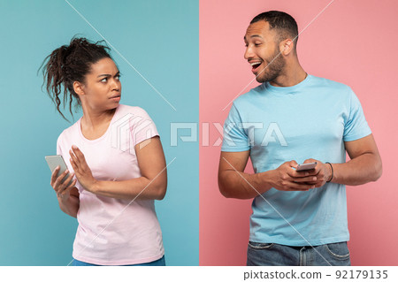 Privacy concept. African american man trying to look at his girlfriend's cellphone, lady hiding screen of her phone 92179135