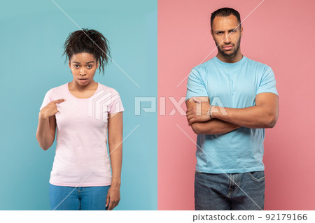 Displeased black lady pointing at herself with wonder, man standing with hands crossed after quarrel Displeased black lady pointing at herself with wonder, man standing with hands crossed after quarrel 92179166