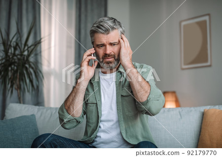Despaired sad elderly european man with beard speaks by smartphone, got bad news in room interior 92179770