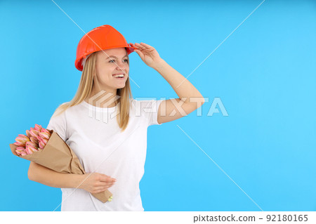 Builder girl with bouquet of flowers on blue background Builder girl with bouquet of flowers on blue background 92180165