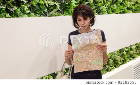 A woman tourist with a map in her hands walks through the big city A woman tourist with a map in her hands walks through the big city 92182553