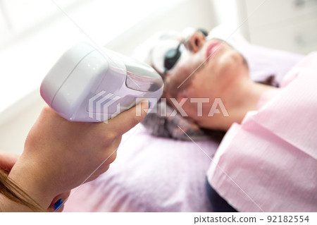 A woman lying on the couch is undergoing a carbon facial peeling procedure A woman lying on the couch is undergoing a carbon facial peeling procedure 92182554