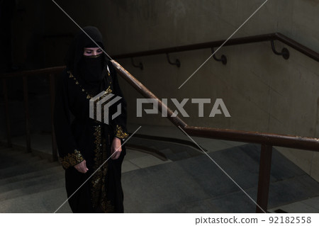 A Muslim woman rises from a dark passage up the stairs, trembling with fear A Muslim woman rises from a dark passage up the stairs, trembling with fear 92182558