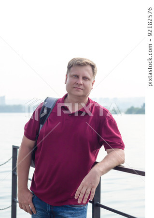 A blond man of model appearance on the beach with a backpack on his shoulder A blond man of model appearance on the beach with a backpack on his shoulder 92182576