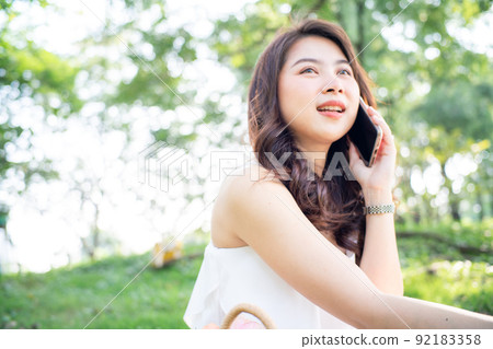 Cheerful young woman talking smartphone in city green park Cheerful young woman talking smartphone in city green park 92183358