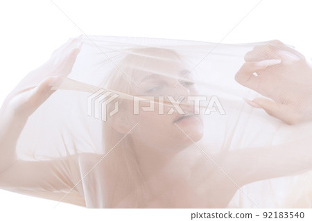 Young tender beautiful girl under transparent fabric, cloth isolated on white studio background. Grace, art, beauty, contemp dance, ad concept. Monochrome 92183540