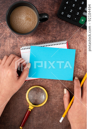 Hands Of Woman Having Pastel Color Paper With Copy Space, Coffee Cup And Stationery Over Wooden Background. Businesswoman Displaying Business Branding And Promotion Ideas. Hands Of Woman Having Pastel Color Paper With Copy Space, Coffee Cup And Stationery Over Wooden Background. Businesswoman Displaying Business Branding And Promotion Ideas. 92184494
