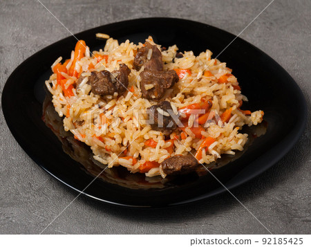 traditional Uzbek pilaf on a black plate on a gray background traditional Uzbek pilaf on a black plate on a gray background 92185425