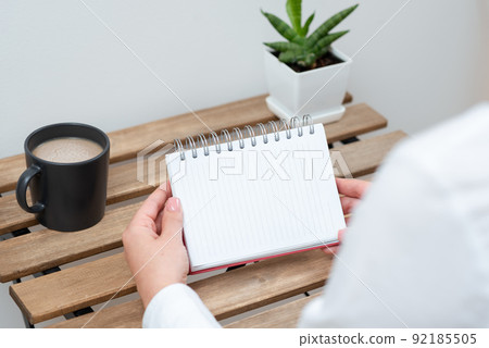 Woman Holding Notebook With Important Message On Table With Coffee And Plant. Businesswoman Presenting Crutial Information On Desk With Cup And Flower. Woman Holding Notebook With Important Message On Table With Coffee And Plant. Businesswoman Presenting Crutial Information On Desk With Cup And Flower. 92185505