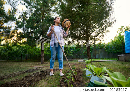 Portrait of a beautiful Hispanic female gardener posing with spade in the organic farm garden, on a hot early spring day 92185917
