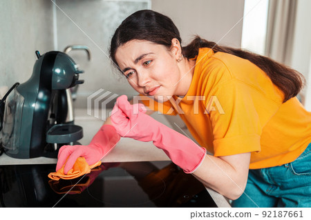Cleaning the house. Portrait of a woman in rubber gloves wiping the cooking surface with a rag, and rubbing dirt in her fingers Cleaning the house. Portrait of a woman in rubber gloves wiping the cooking surface with a rag, and rubbing dirt in her fingers 92187661